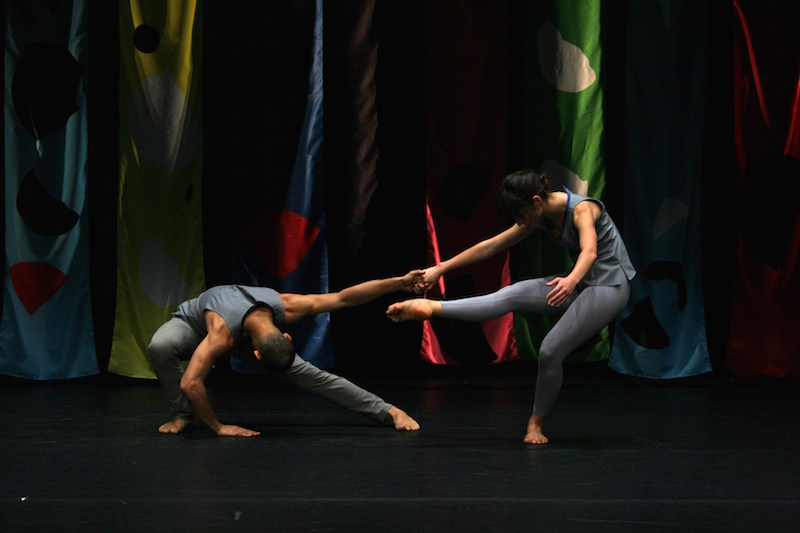 Two Compagnie CNDC-Angers  dancers counterbalance against one another; one is balancing on one foot with her torso to the floor while the other is in a deep lunge. 